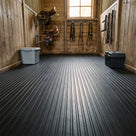 Timber tack room with saddles and bridles on the walls, floor covered in black wide rib rubber matting